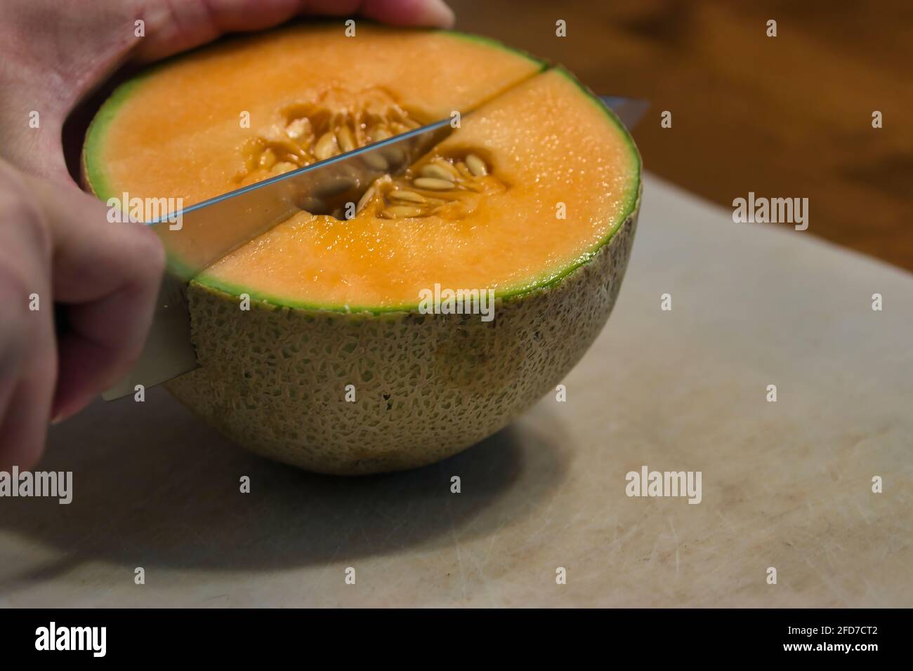 hand cutting half a cantaloupe into quarter wedges on cutting board Stock Photo