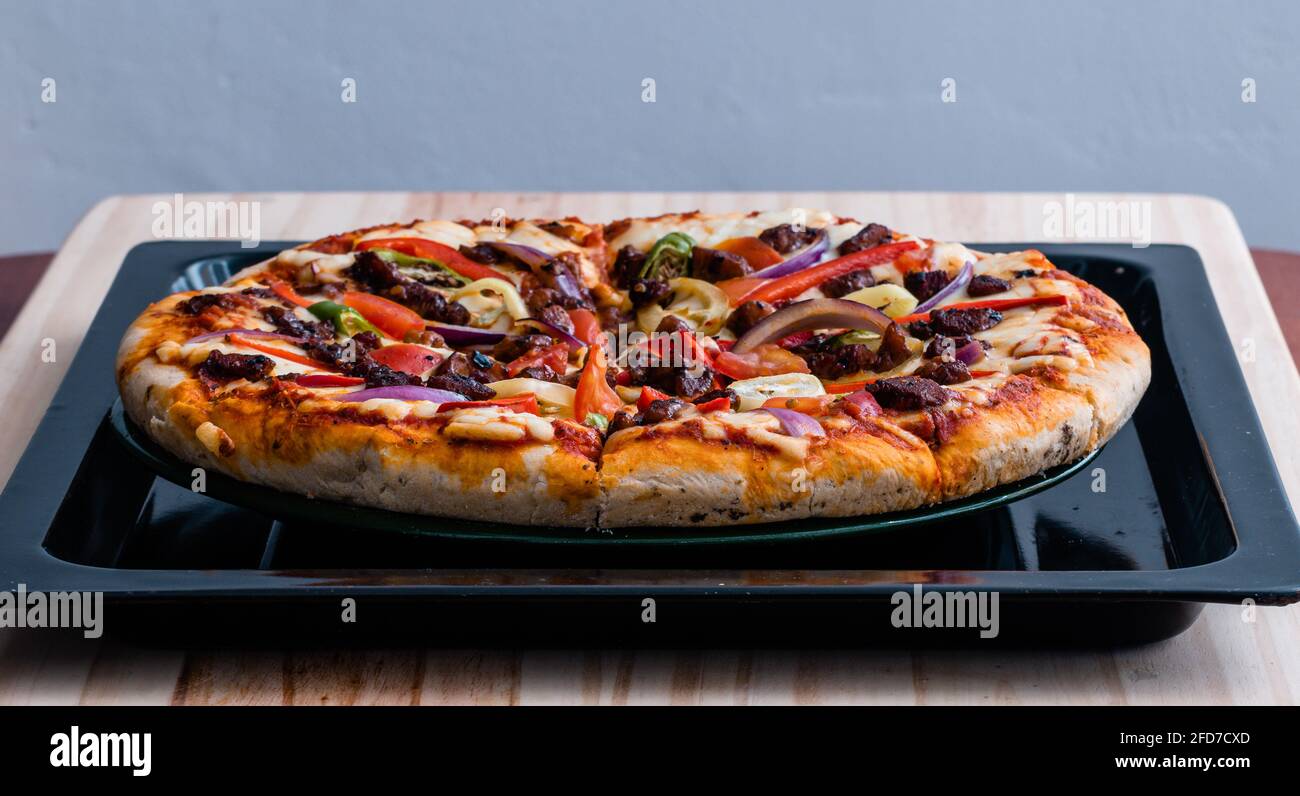 Hot pizza was taken out from the oven, homemade and delicious fast food, sliced while in the oven tray and ready to eat, chicken cheese, and colorful Stock Photo