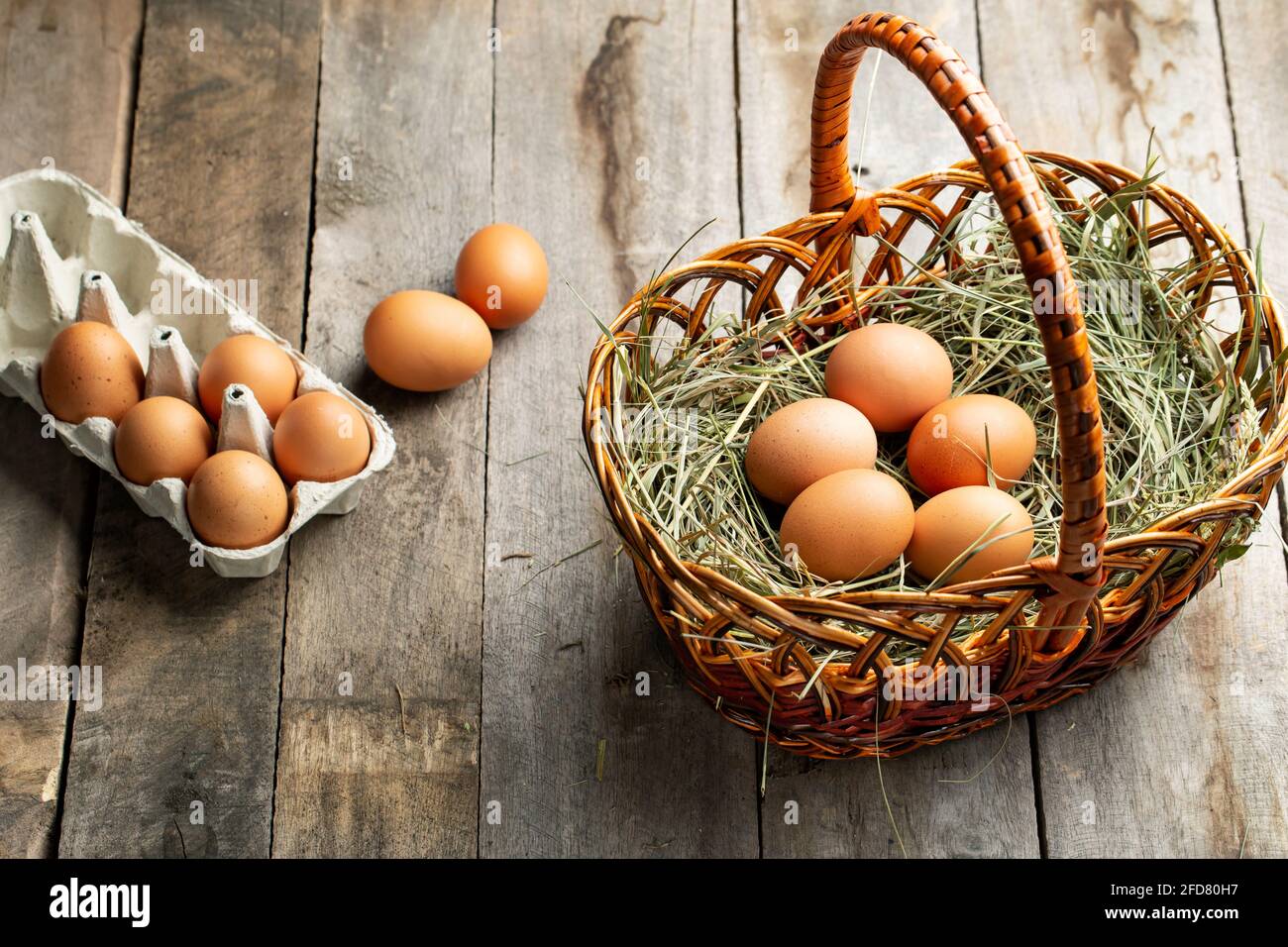 Chicken eggs in a hay basket and egg tray, on a wooden table ...