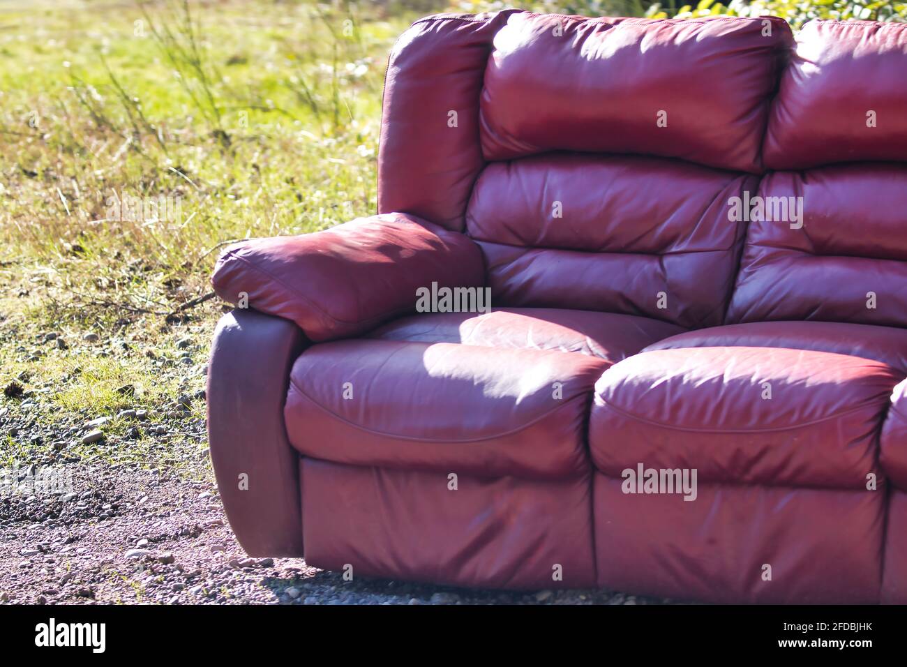 red leather couch dropped in the dirt off the side of the road Stock