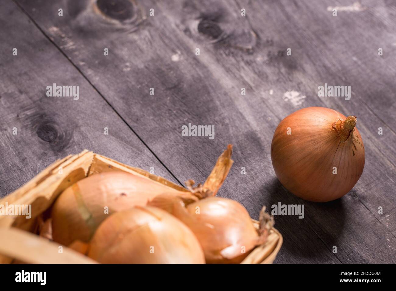 Brown onions in basket on wooden background. Stock Photo
