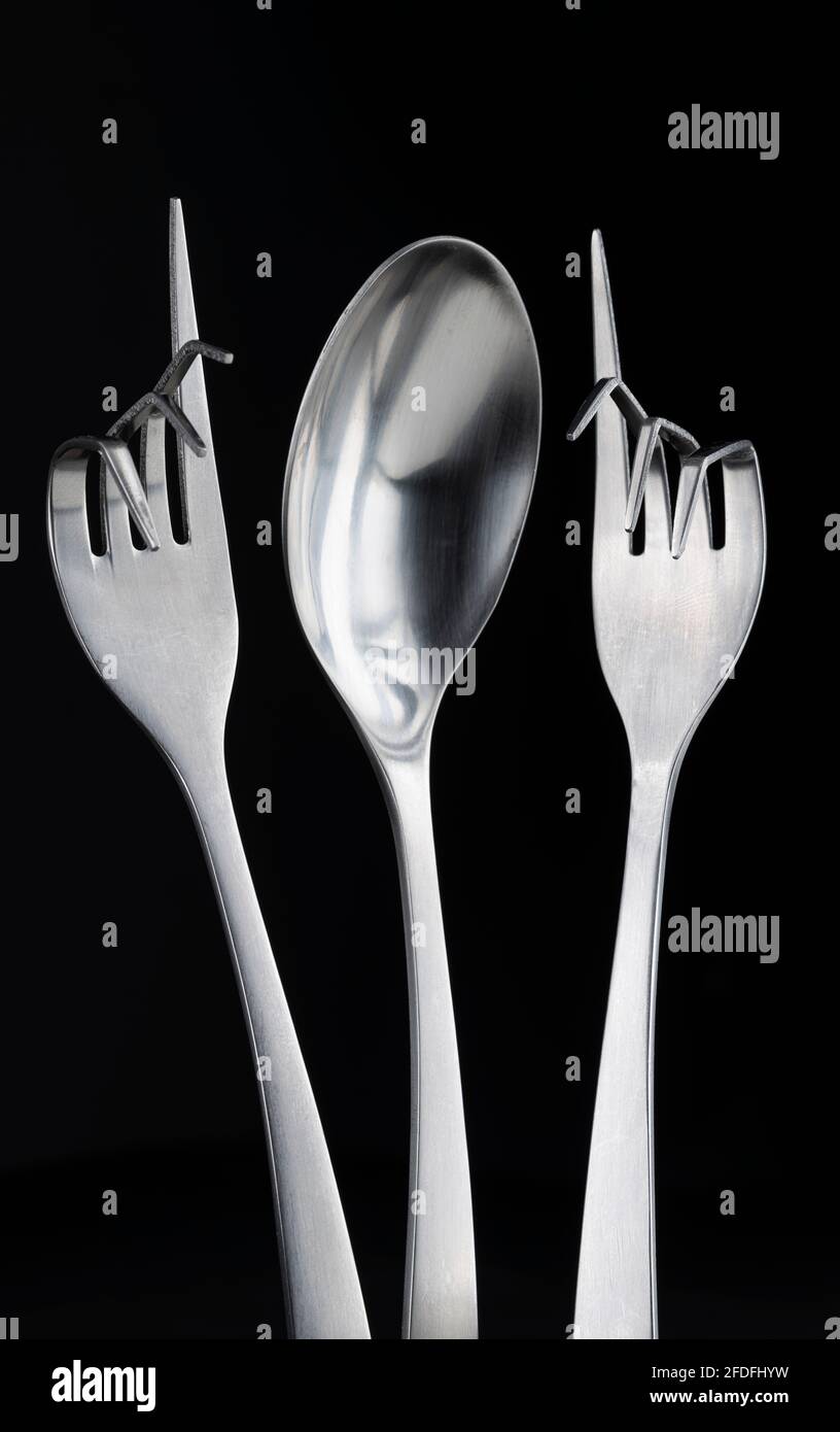 Conceptual figure of a stainless steel spoon and two stainless steel curved forks against a black background Stock Photo