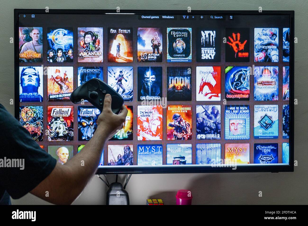 Man holding a steam controller in front of the steam good old games gog  epic store library screen choosing a game to play for entertainment leisure  Stock Photo - Alamy