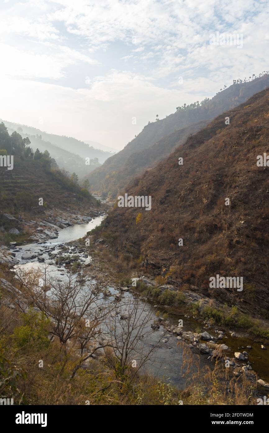 A river flowing through a narrow valley with stones and rocks scattered and mountain ranges with sky in the horizon Stock Photo