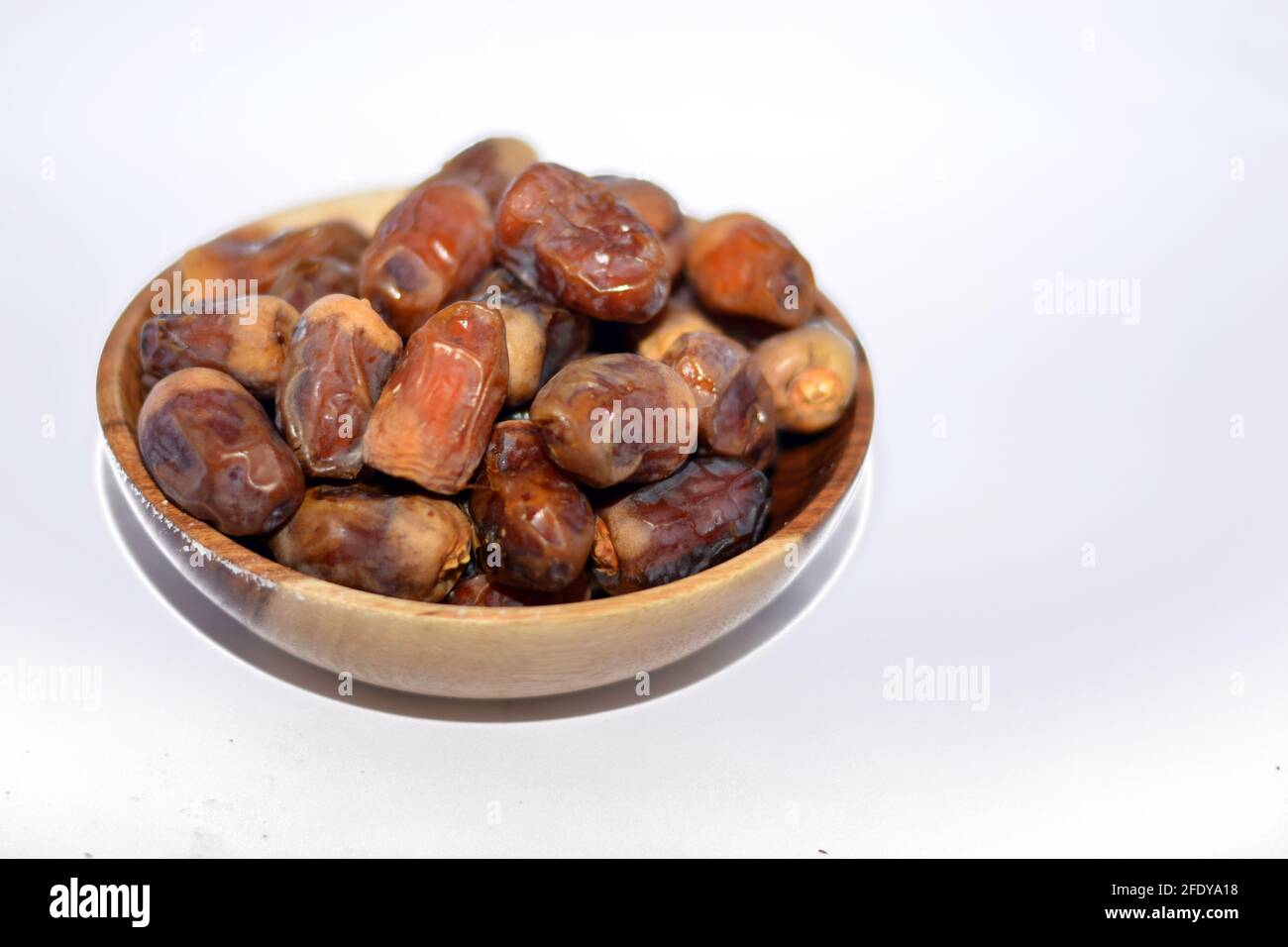 Dried dates fruit in a wooden bowl isolated on a white background, dried dates used in breakfast in Ramadan month as the first iftar meal Stock Photo