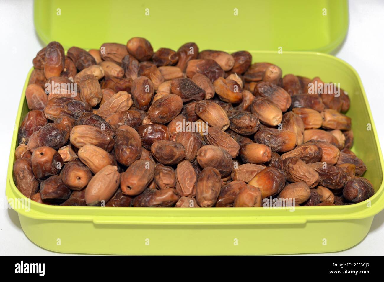 Dried dates fruit in a green plastic food container isolated on a white background, dried dates used in breakfast in Ramadan month as the first iftar Stock Photo