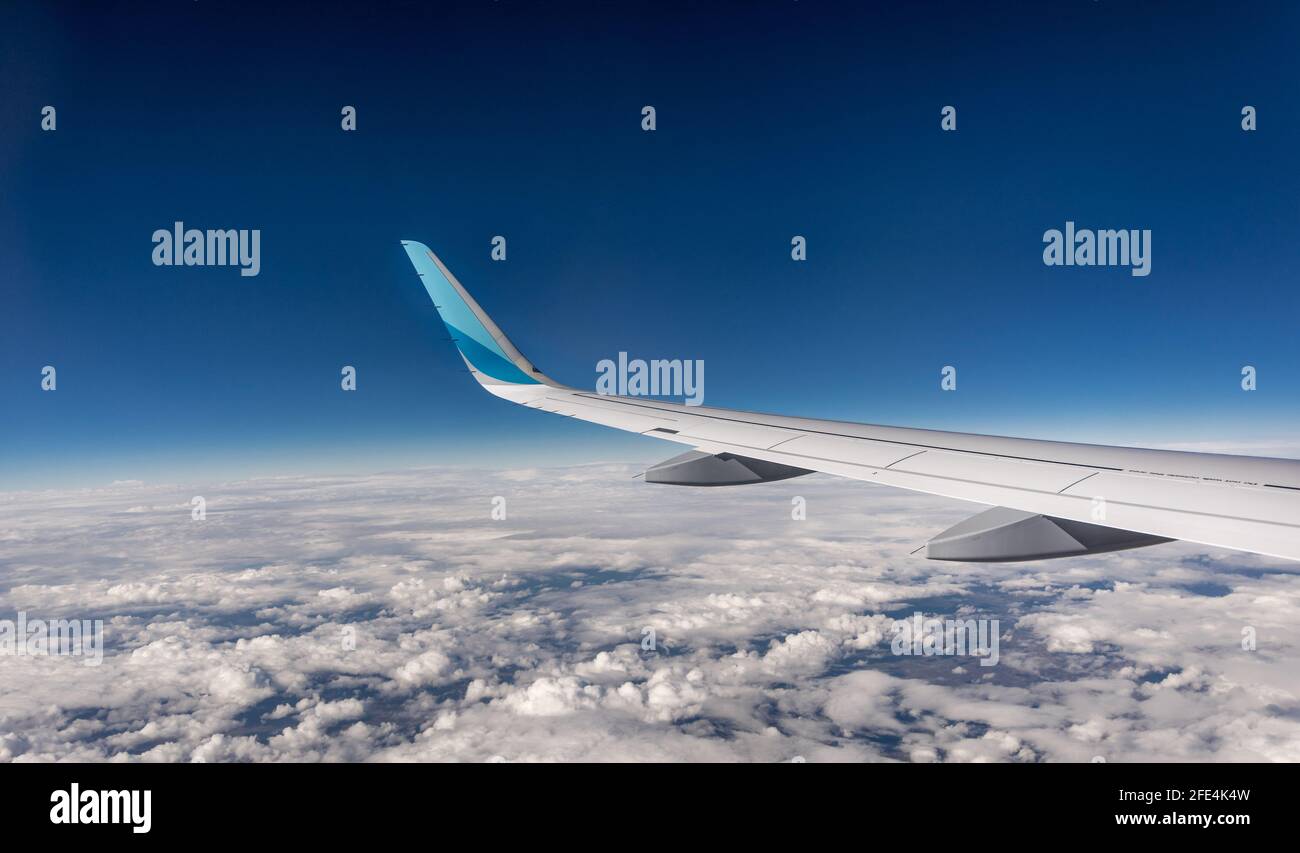 Wing of airplane from window during flight. Blue sky with soft white clouds Stock Photo