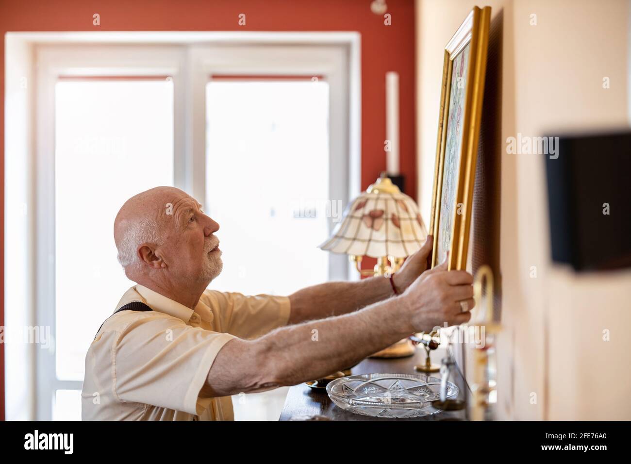 Senior man putting up a painting on the wall at his home Stock Photo