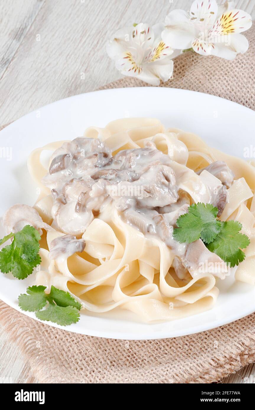 Fettuccine with mushrooms in a creamy sauce with a sprig of herbs. Italian dish. Stock Photo