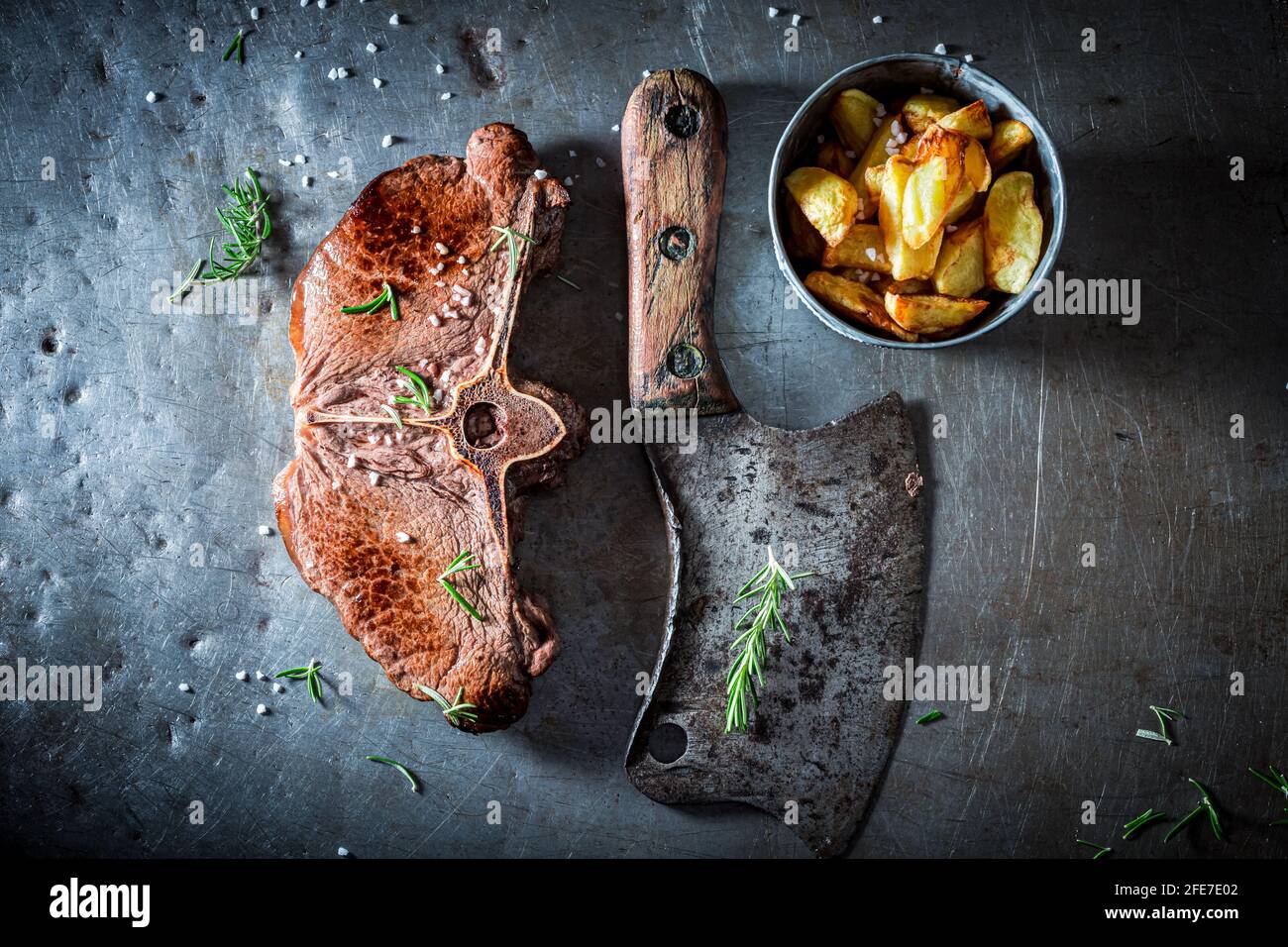 Steak and chips on metal table with rosemary. Well done steak and chips