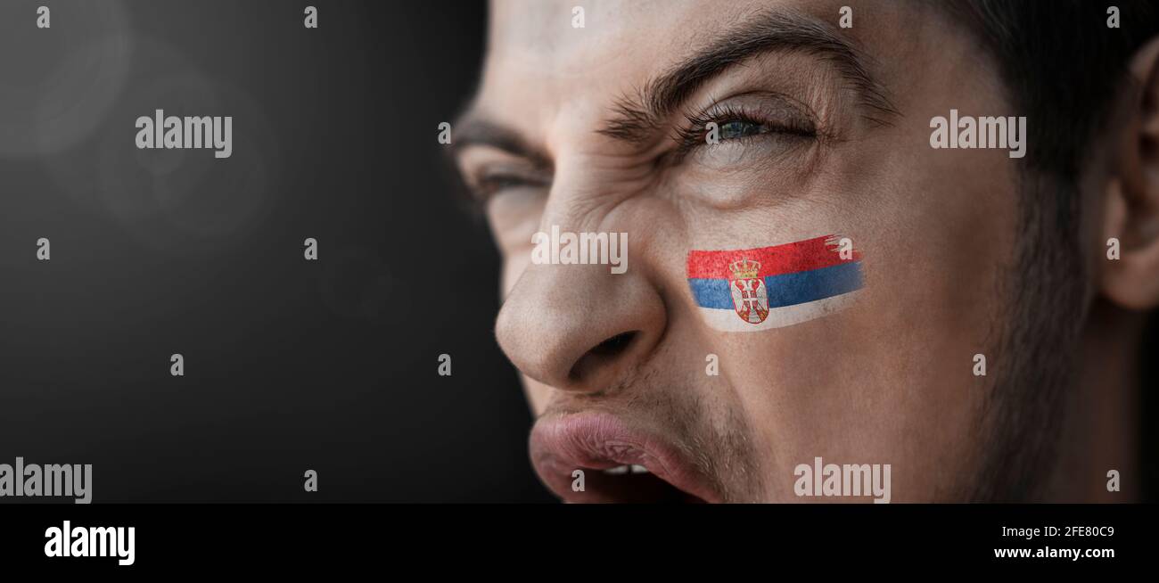 A screaming man with the image of the Serbia national flag on his face Stock Photo