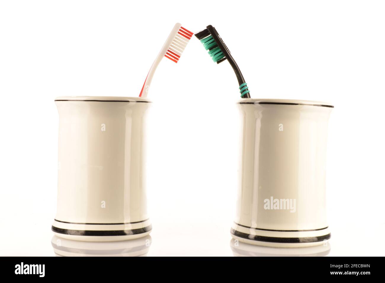 Two toothbrushes in a light ceramic glass on a white background. Stock Photo