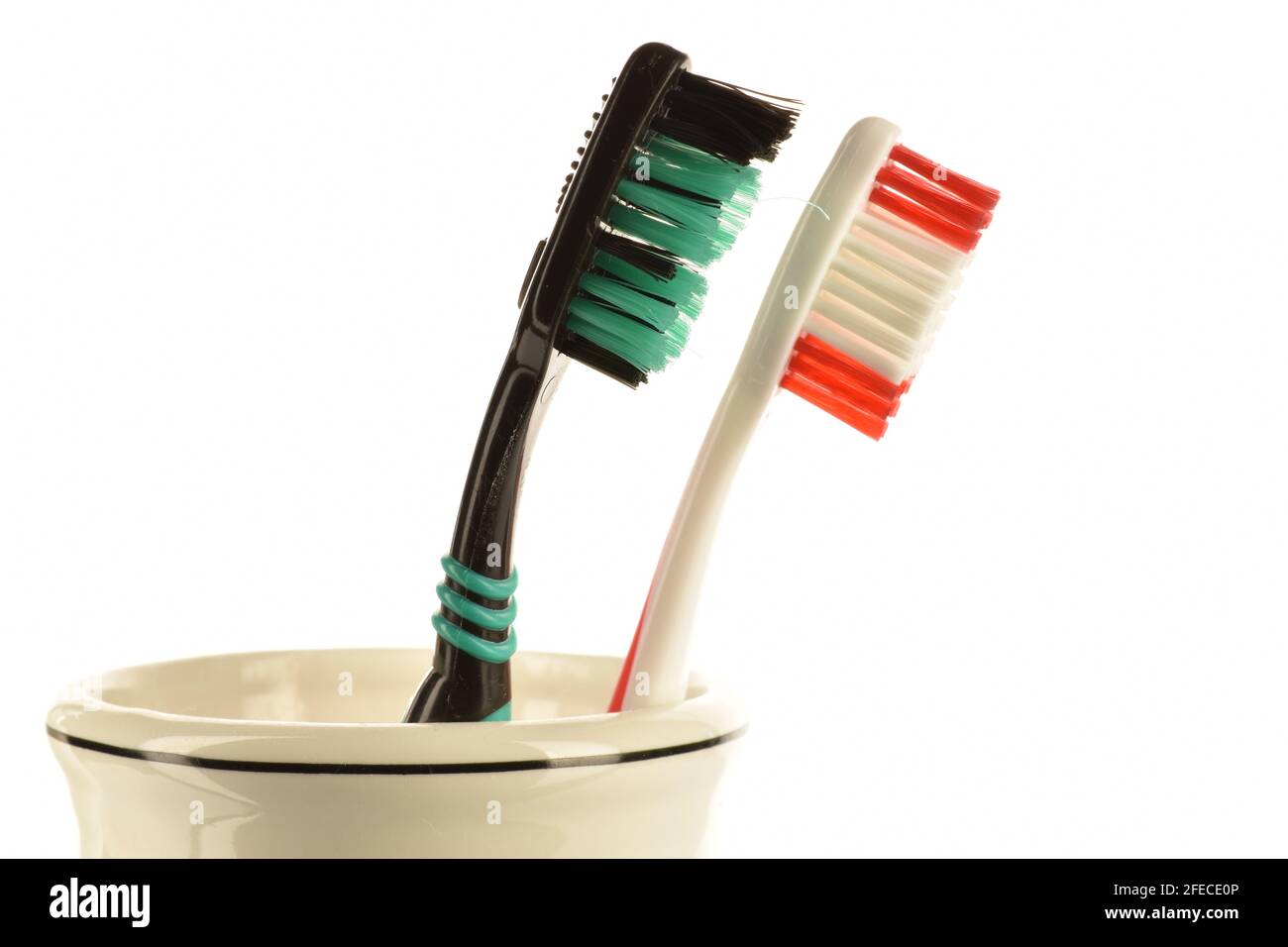 Two toothbrushes in a light ceramic glass on a white background. Stock Photo