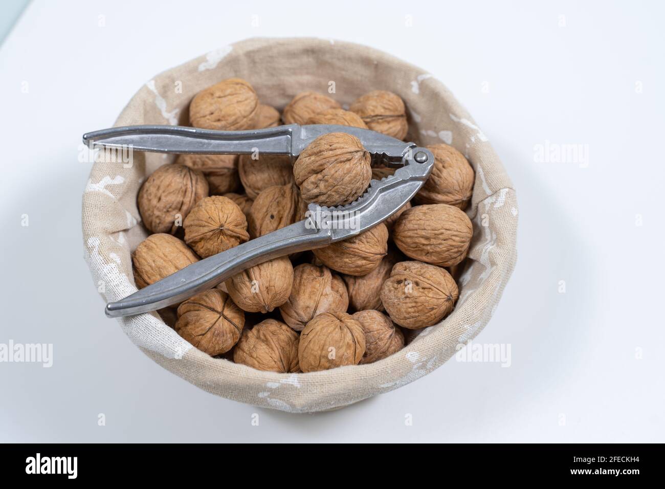 basket with whole walnuts and nutcracker on a white background, top view Stock Photo