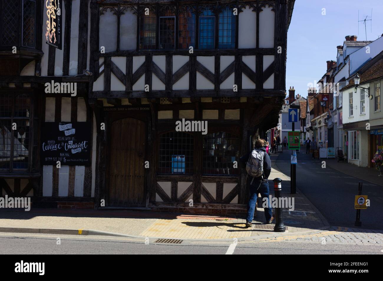 Rear view of a young man carrying a rucksack crossing the street towards the historic Cross Keys Hotel building, Saffron Walden, Essex, Britain, April Stock Photo