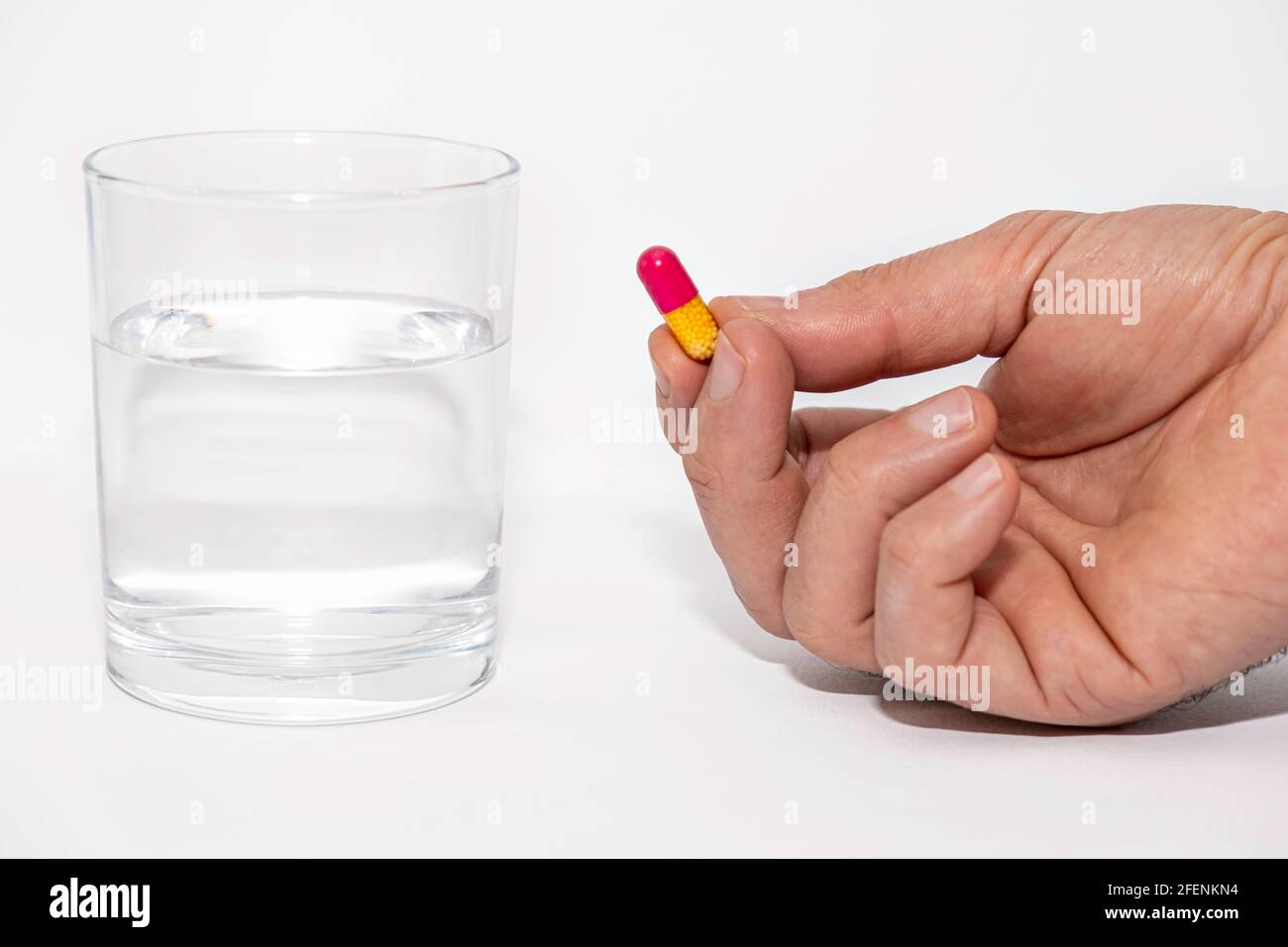 close up of male hands holding pill capsule vitamin supplement with glass of water on white background close up Stock Photo
