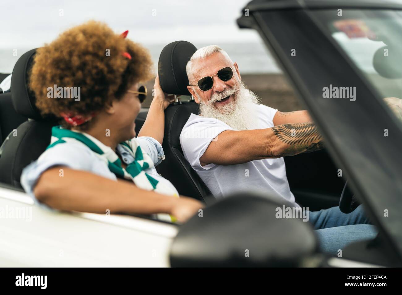 Happy senior couple having fun driving on new convertible car - Mature people enjoying time together during road trip tour vacation Stock Photo
