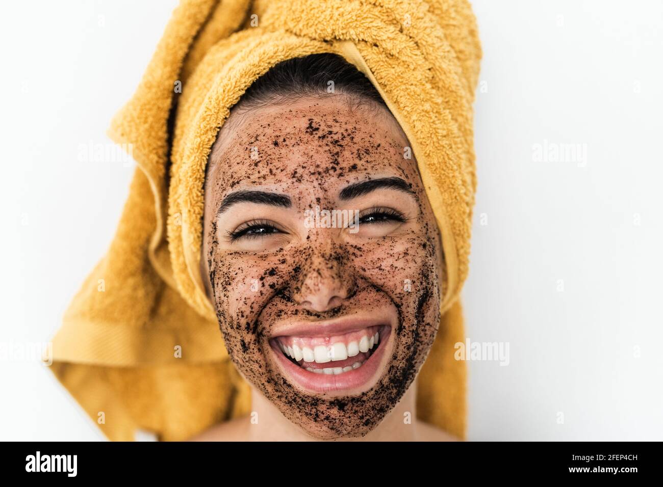 Young smiling woman applying coffee scrub mask on face - Happy girl having skin care spa day at home Stock Photo