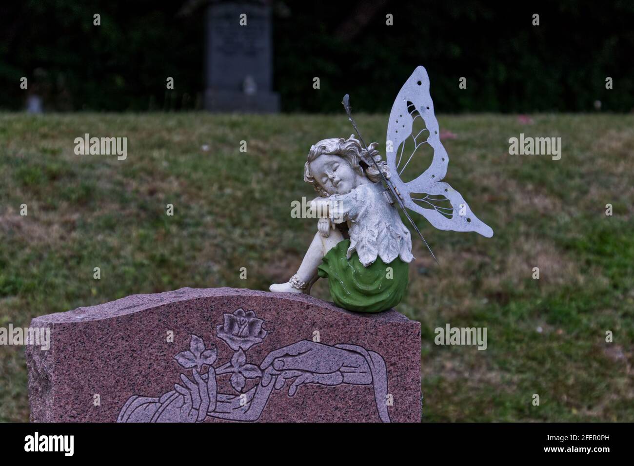 Sweet angel figurine on top of a headstone in a church graveyard - green grass background Stock Photo