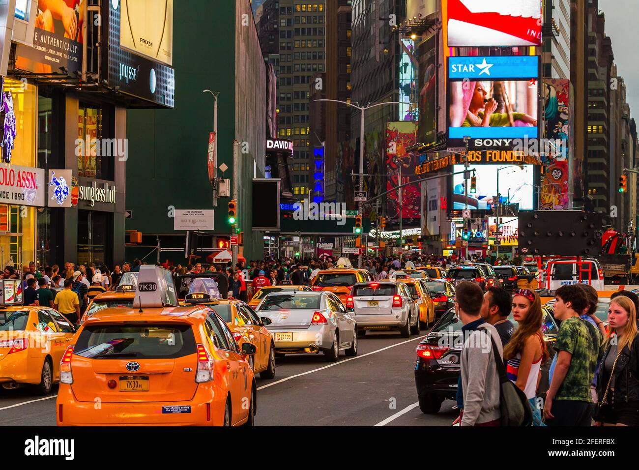 Heavy traffic with cars and taxi cabs and tourists crossing the road on a busy evening at Times Square Stock Photo