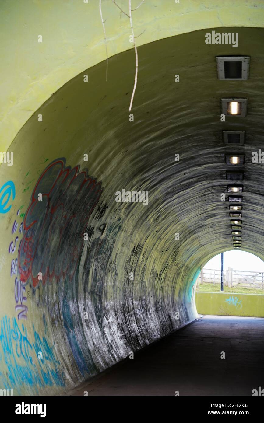 Subway, under-pass, floodlights, scary, night-time, lone traveller, short-cut, round tunnel, link footway, concrete, graffiti, wall art, Banksy, tag. Stock Photo