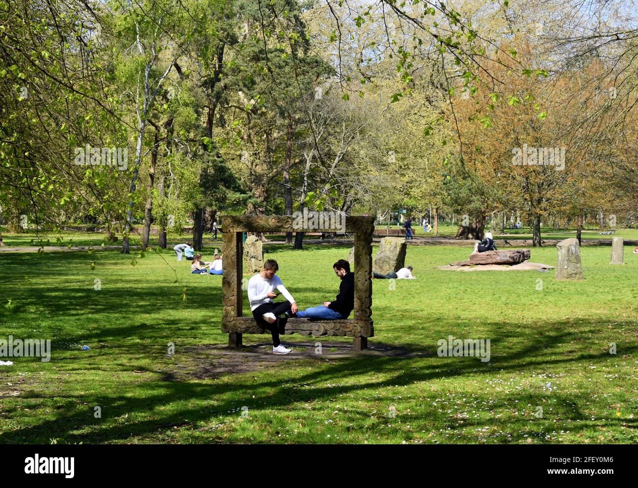 Two men sitting in the wooden picture frame sculpture in front of the Gorsedd stone circle, Bute Park, Cardiff, Wales Stock Photo