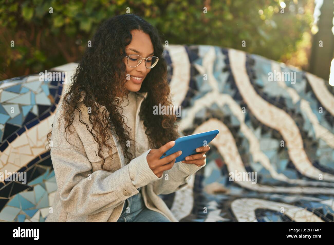 Young latin woman smiling happy using touchpad sitting on the bench at ...