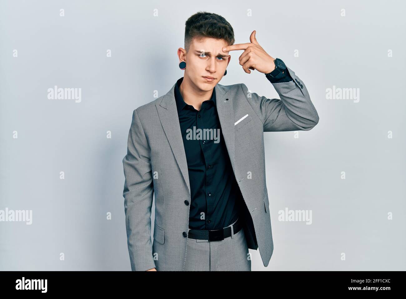 Young caucasian boy with ears dilation wearing business jacket pointing unhappy to pimple on forehead, ugly infection of blackhead. acne and skin prob Stock Photo