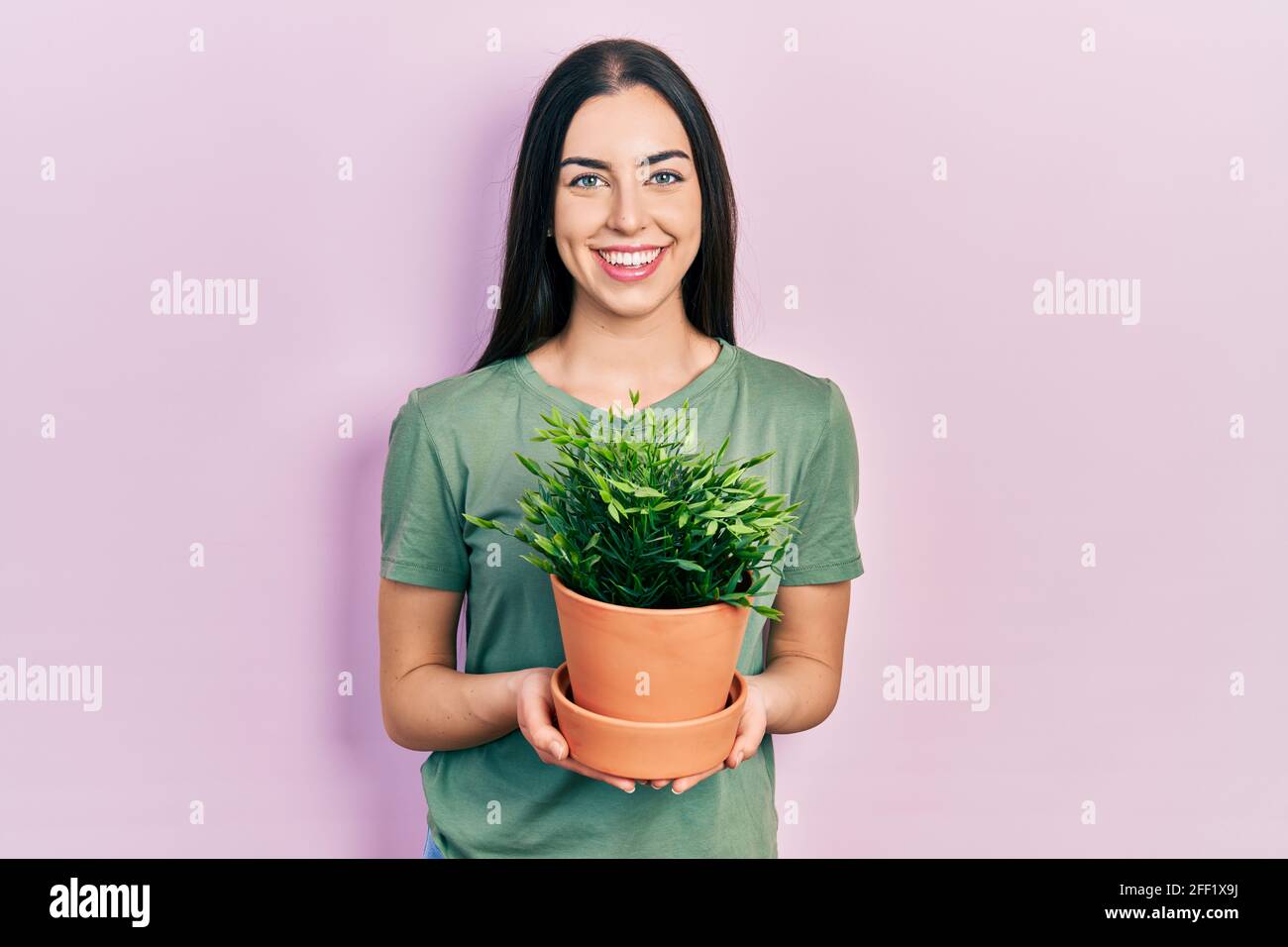 Beautiful woman with blue eyes holding green plant pot smiling with a ...
