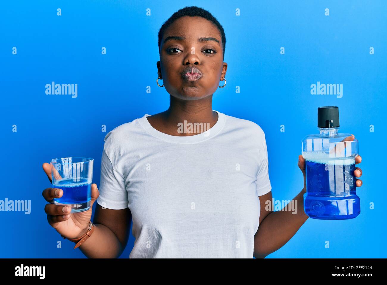 Young african american woman holding mouthwash for fresh breath puffing