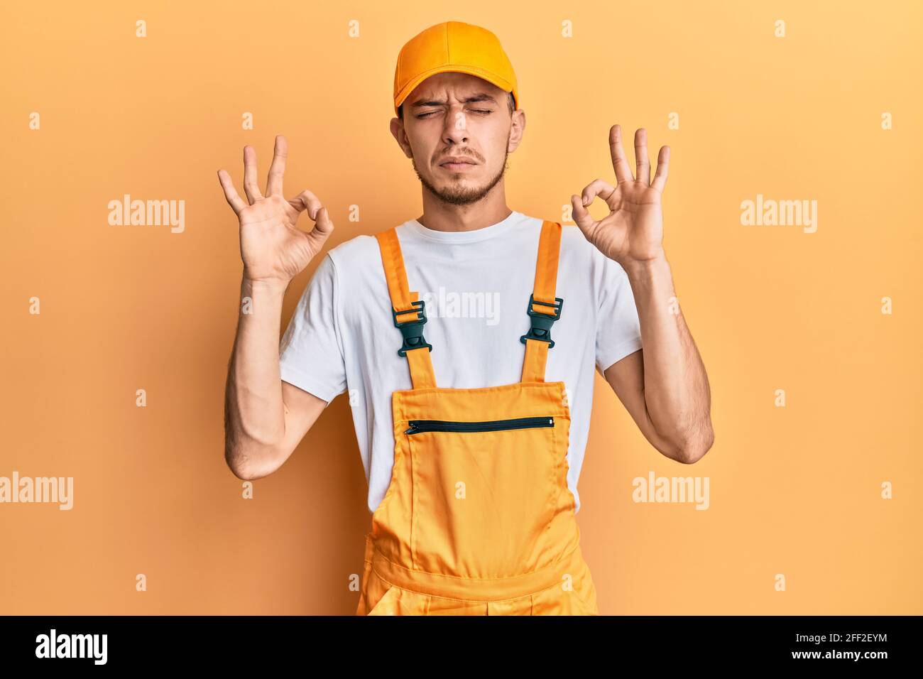 Hispanic young man wearing handyman uniform relaxed and smiling with ...