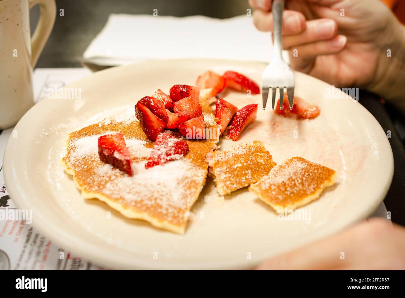 A patron at a diner finishes her pancakes with fresh strawberries and granulated sugar. Stock Photo