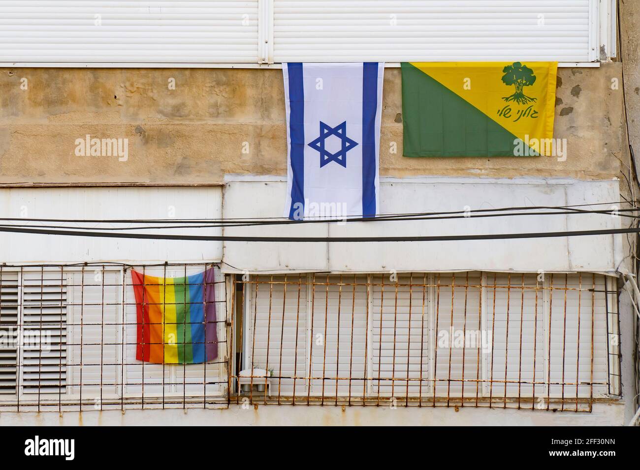 Tel Aviv, Israel - April 16th, 2021: Three flags on an old building in Tel Aviv: the israeli national flag, the rainbow flag, and the flag of 'Golani' Stock Photo