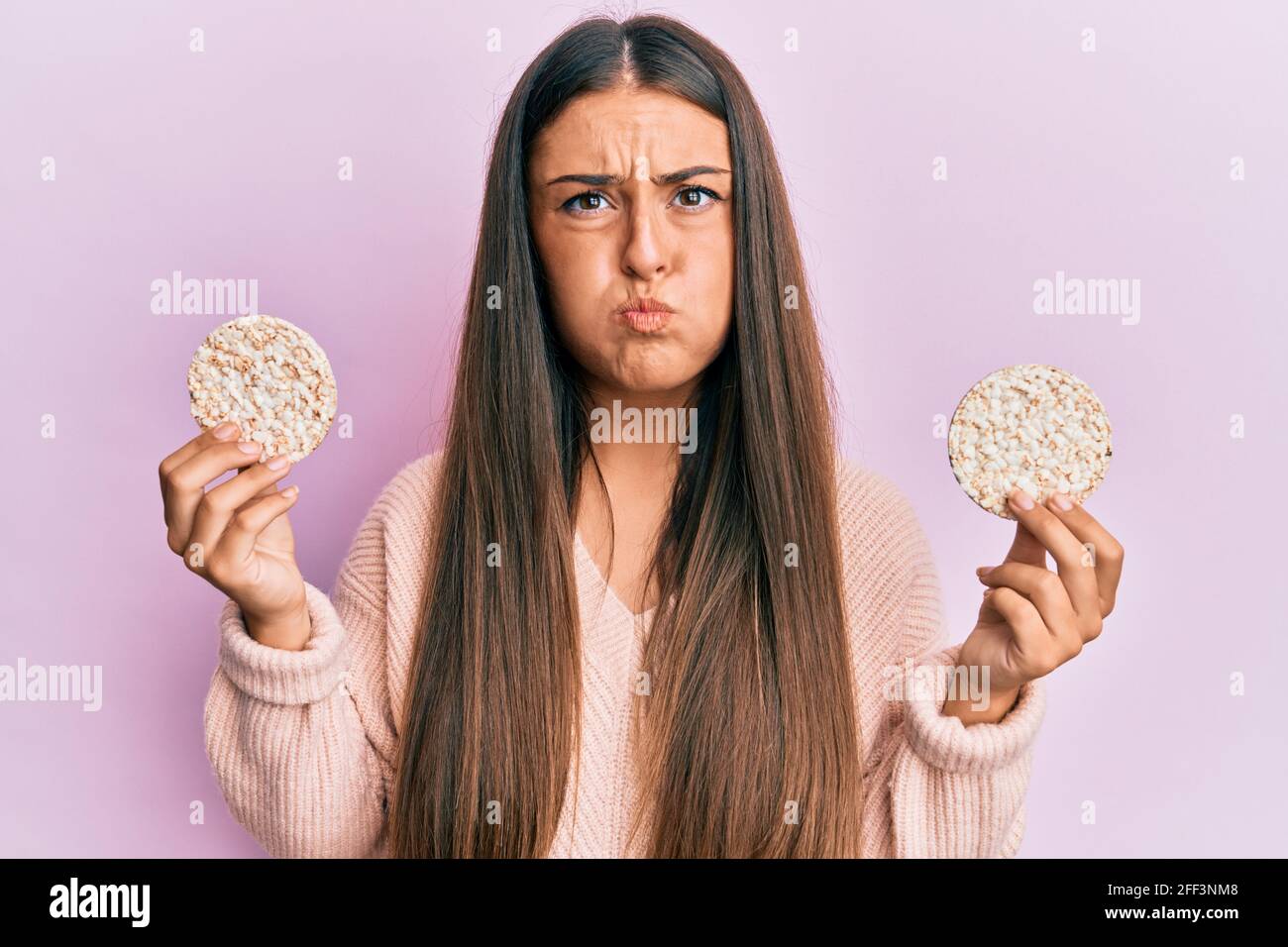 Beautiful hispanic woman eating healthy rice crackers puffing cheeks with  funny face. mouth inflated with air, catching air Stock Photo - Alamy
