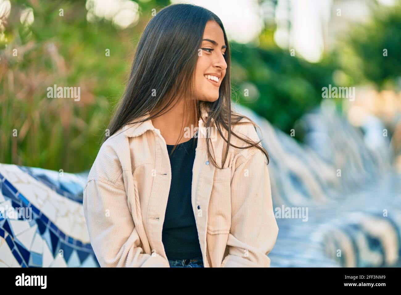 Young hispanic girl smiling happy sitting on the bench at the park ...