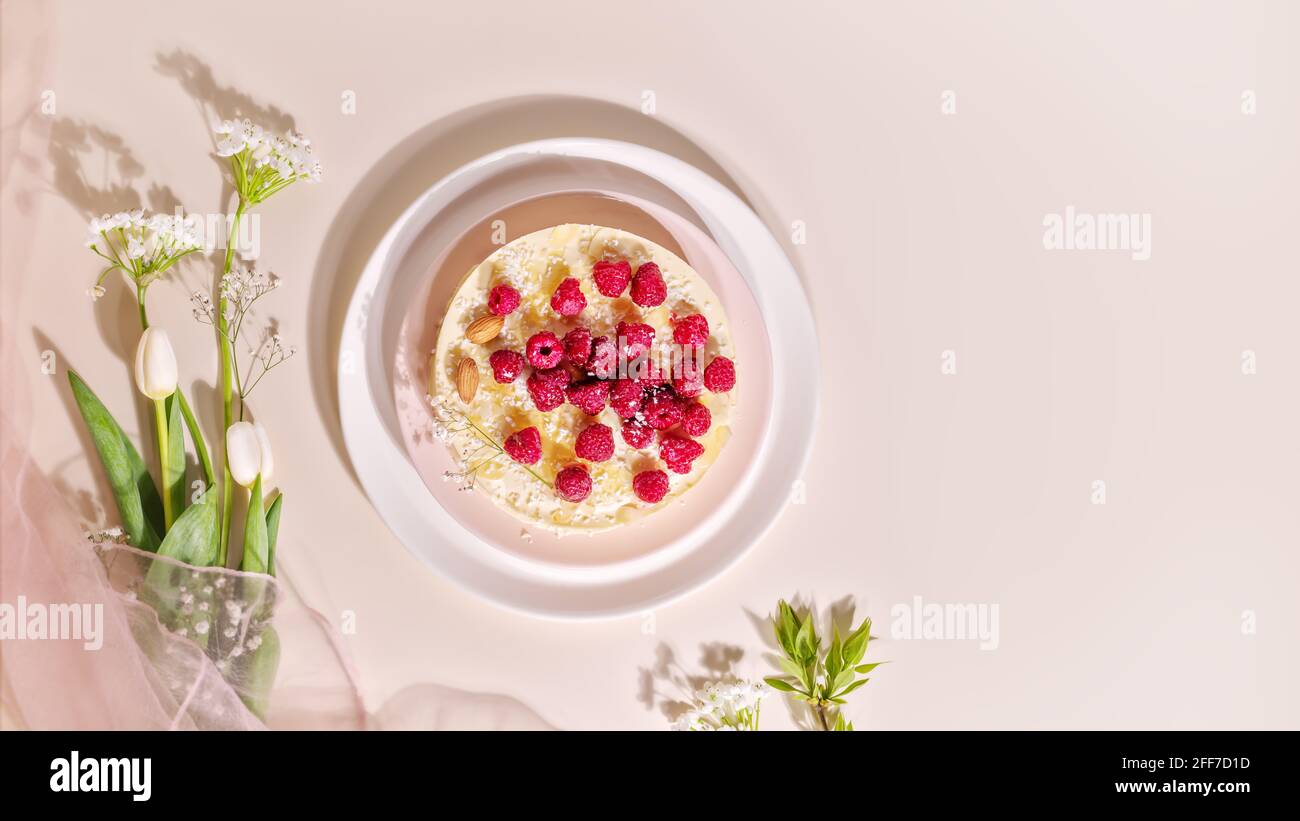 Food composition with raspberry almond cake with and spring bouquet with tulips on a pink background. Sweet pastries with almond flour are gluten-free Stock Photo