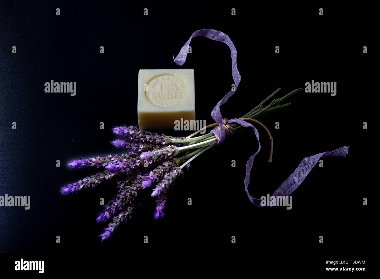 Bar of soap that has written in French 'Pure vegetable, 125 grams, made in France' with a bouquet of lavender flowers tied with cream-colored rope and Stock Photo