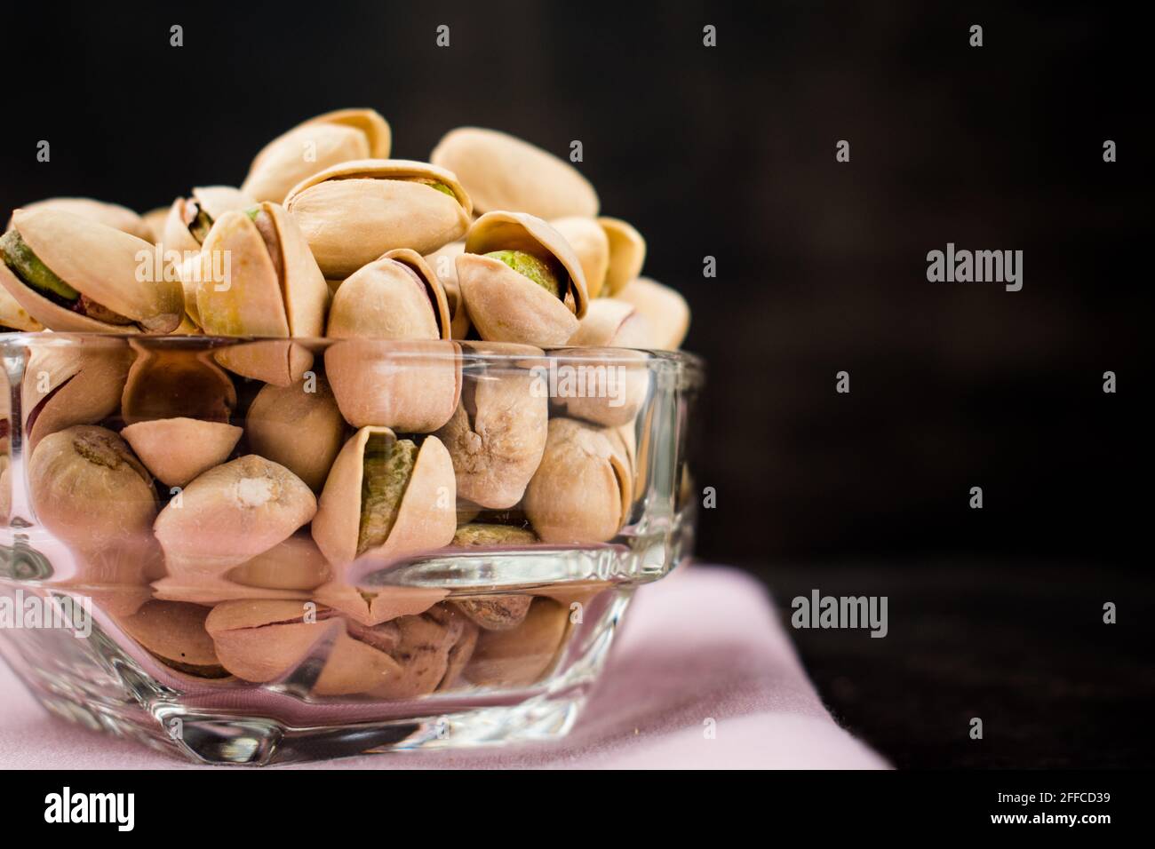 Some pistachios in a glass bowl on a black wooden table Stock Photo