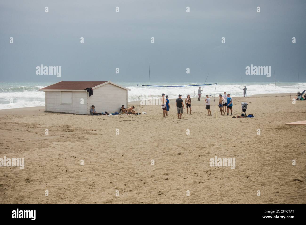 Group of teenagers on the beach playing volleyball, with rain clouds
