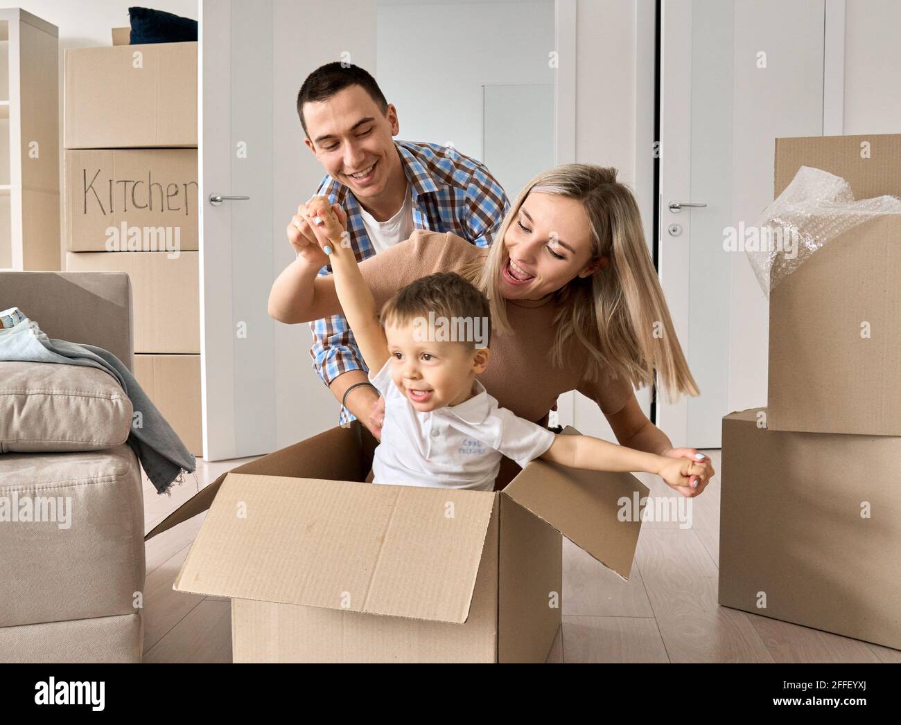 Happy joyful parents and kid ride carton box in new mortgage apartments. Stock Photo