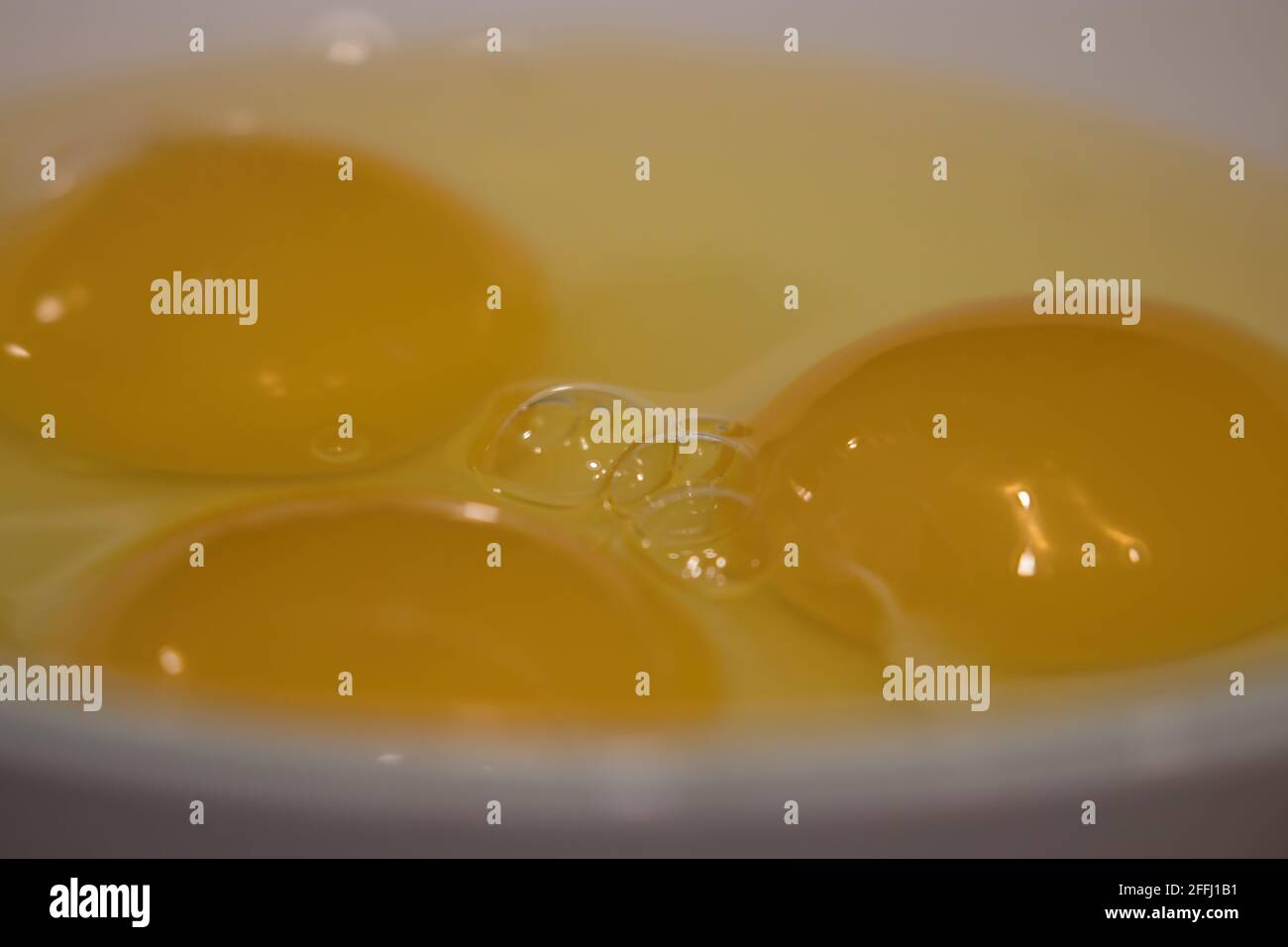 three raw eggs cracked into a plain white bowl Stock Photo