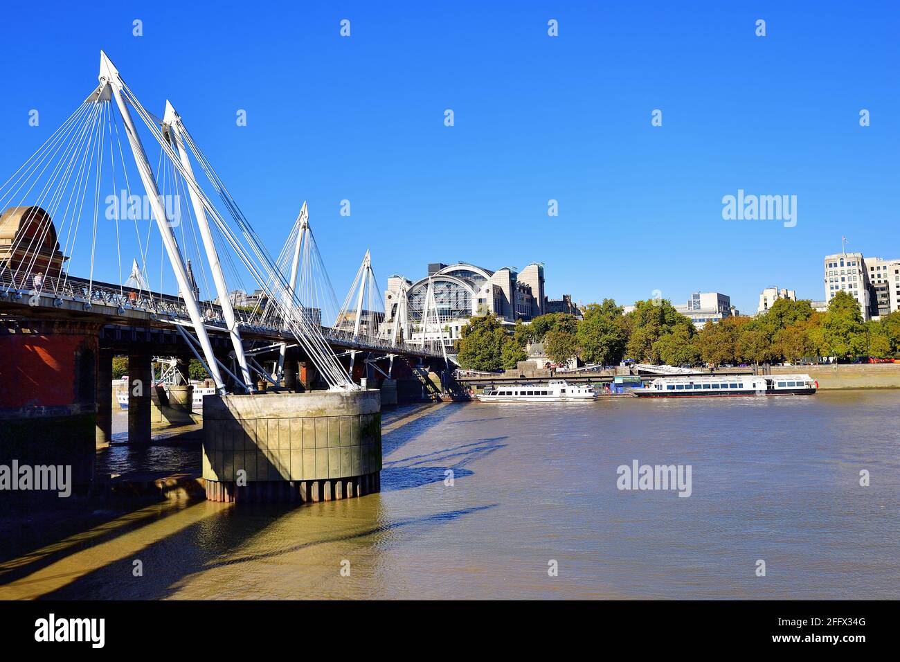 London, England, United Kingdom. Boats tied up at piers along the Embankment sit stationary in the River Thames next to the Golden Jubilee Bridge. Stock Photo