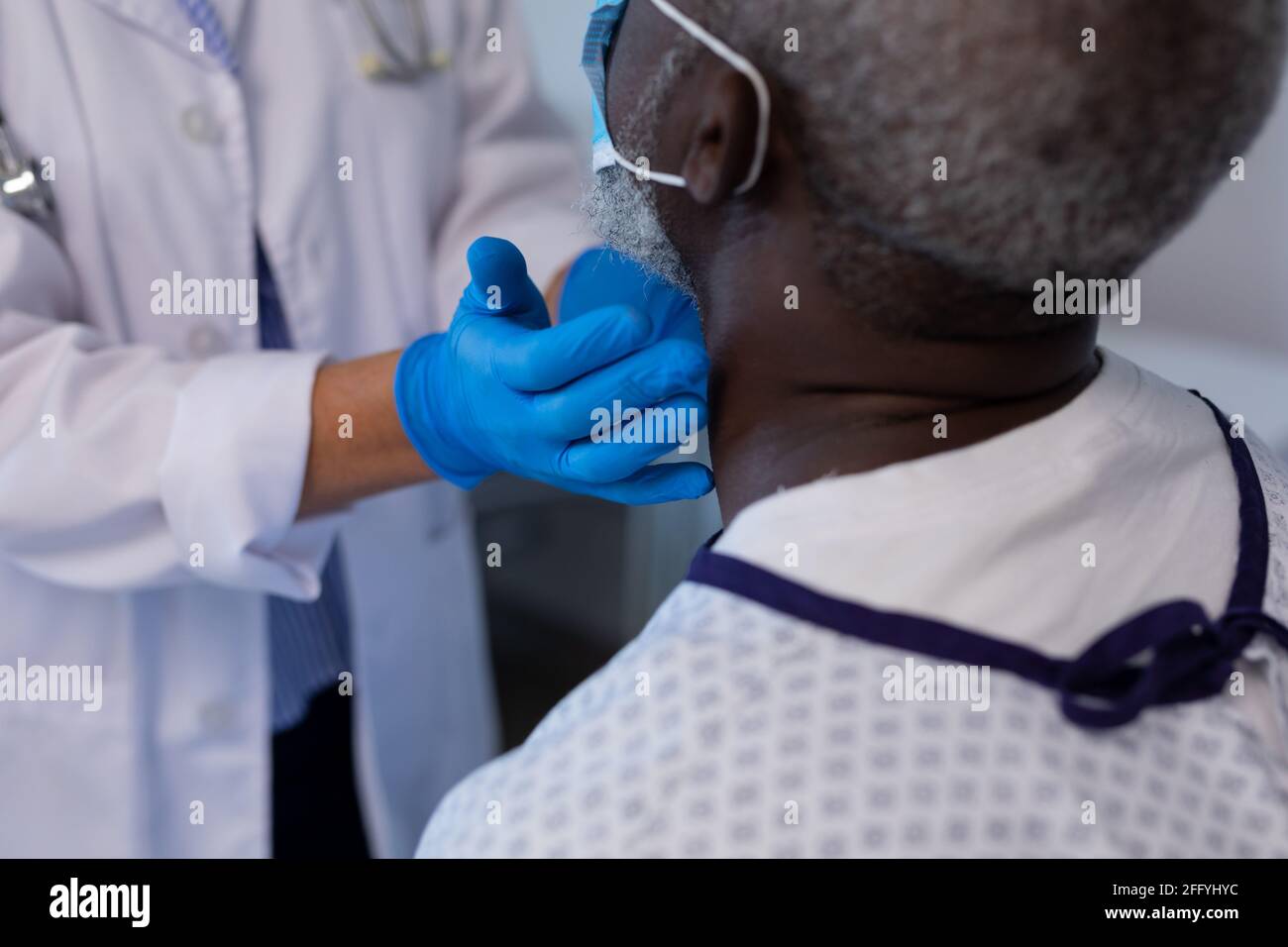 Caucasian female doctor palpating lymph nodes of african american male patient wearing mask Stock Photo