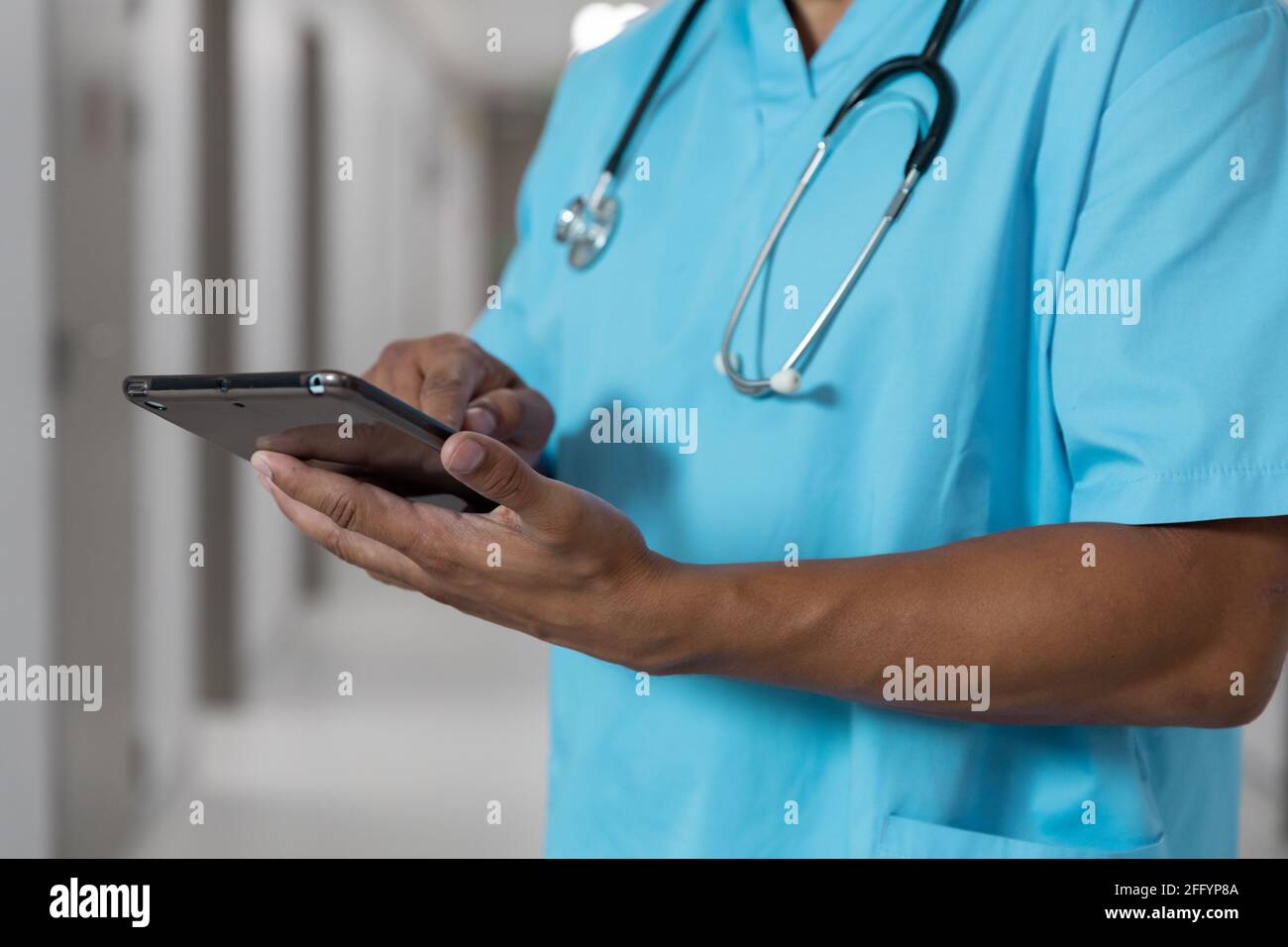 Midsection of mixes race male doctor standing in corridor using tablet Stock Photo
