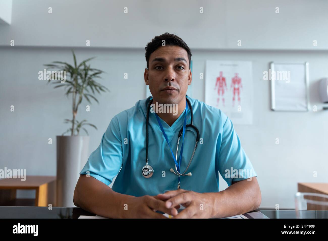 Mixed race male doctor at desk talking and gesturing during video call consultation Stock Photo