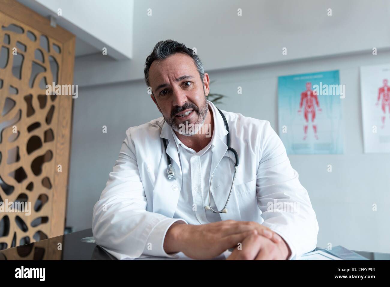 Mixed race male doctor at desk talking and gesturing during video call consultation Stock Photo