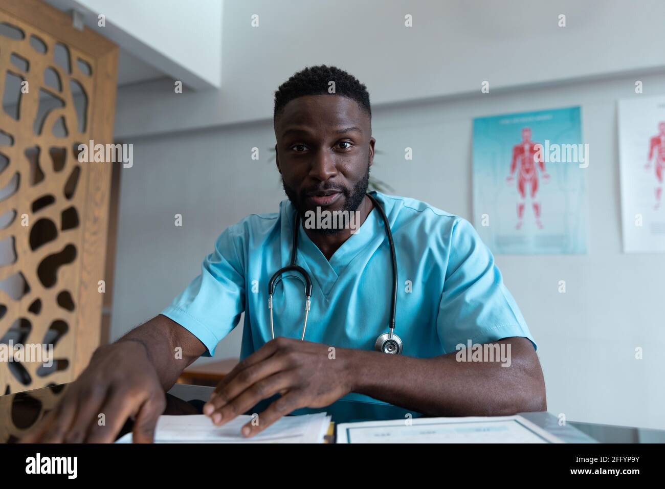 African american male doctor at desk talking and gesturing during video call consultation Stock Photo