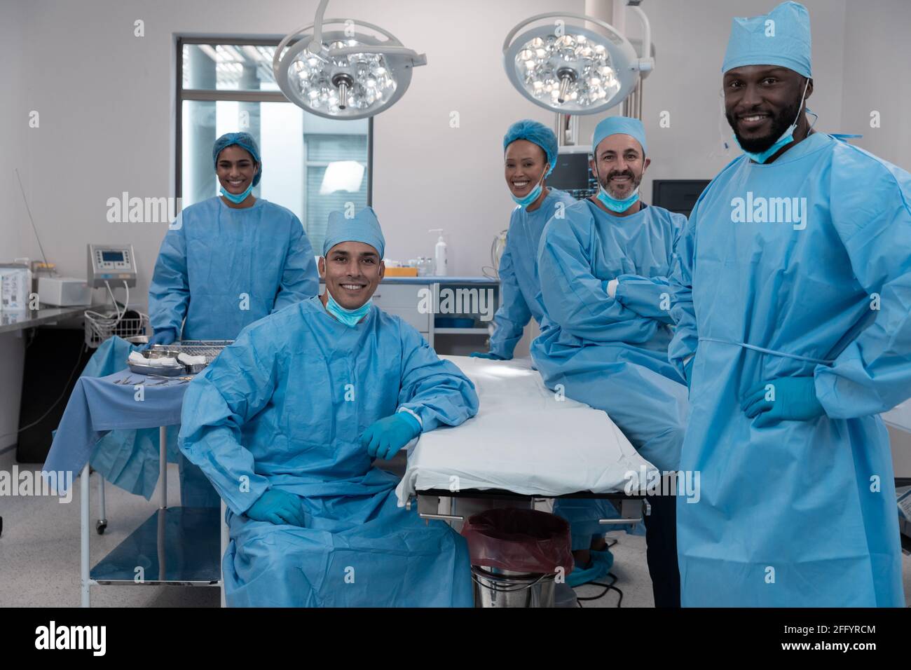 Smiling diverse surgeons with face masks and protective clothing in operating theatre Stock Photo