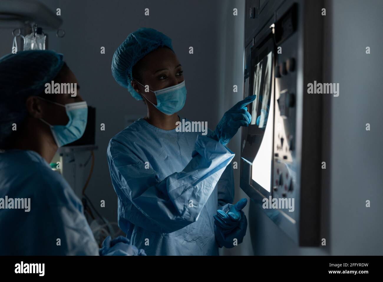 Diverse female doctors wearing face masks and surgical overalls looking at lung x-ray Stock Photo