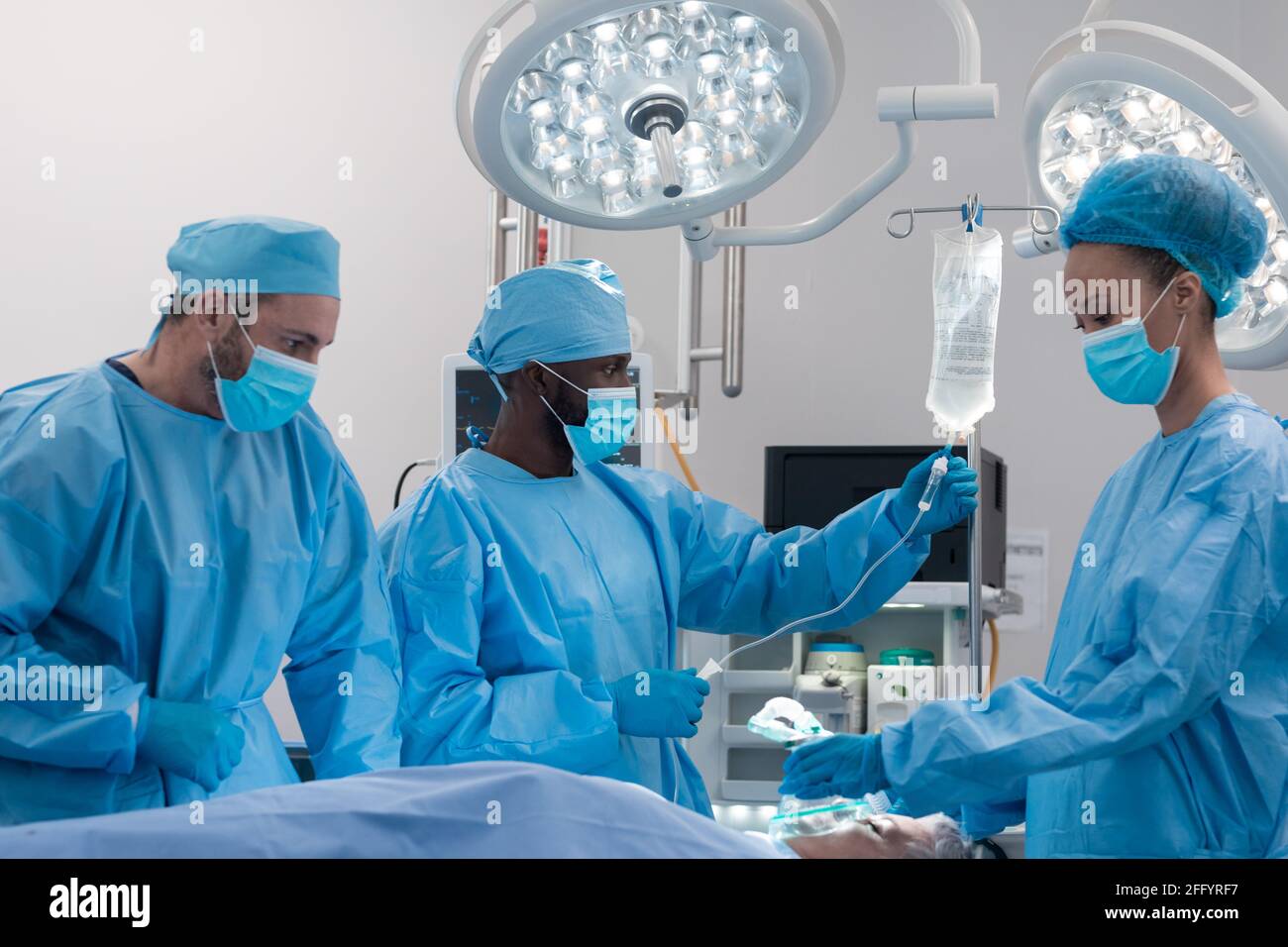 Diverse male and female doctors wearing face masks and surgical overalls in operating theatre Stock Photo